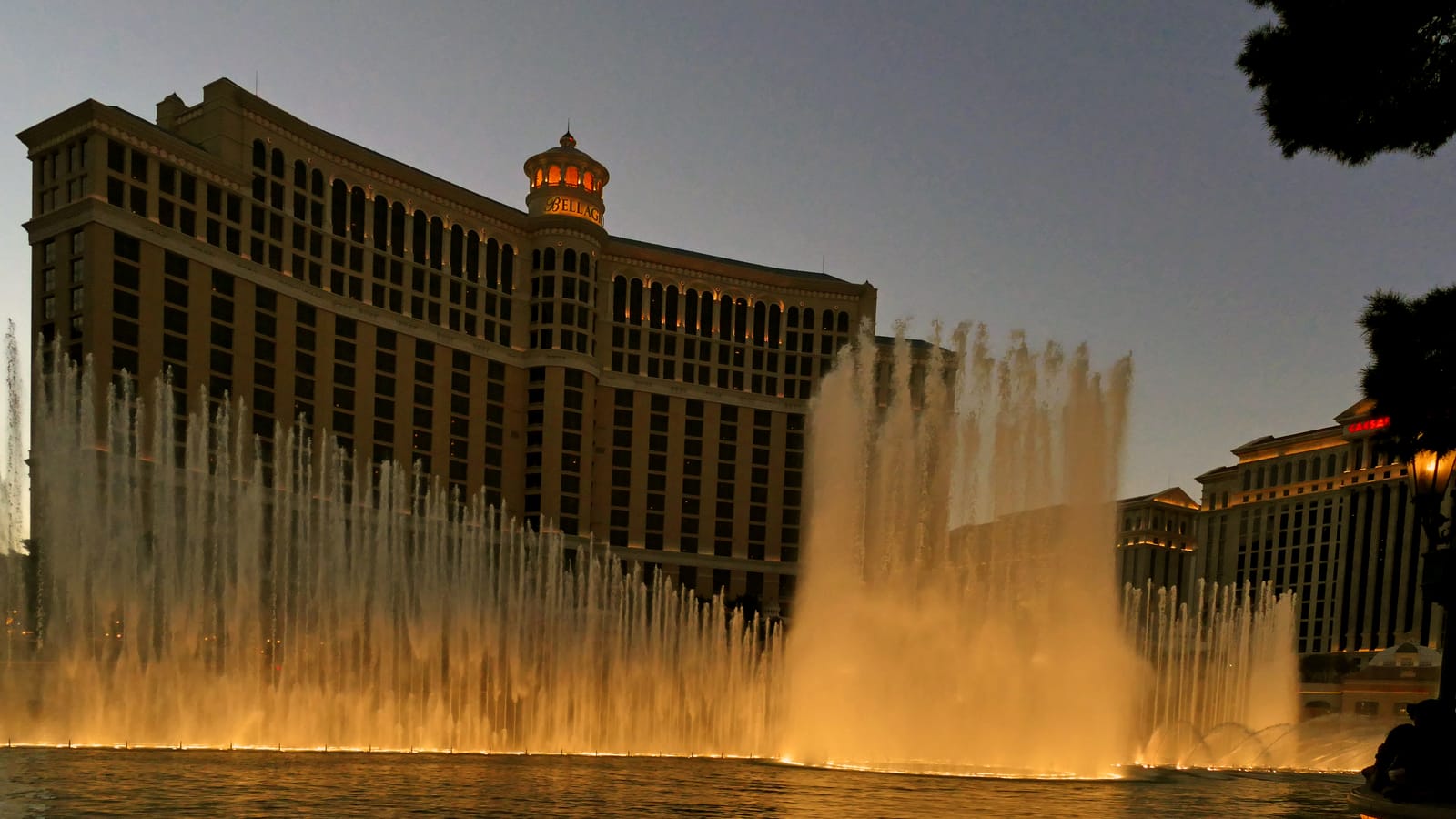 The Fountains of Bellagio in full display at dusk, with the Bellagio tower behind the lake